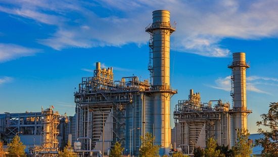 Massive gas fired power plant near a long mountain range on a sunny day.